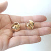 Round gold earrings held in a hand against a white background