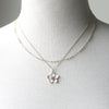 A double-strand necklace displayed on a white fabric mannequin bust. The necklace features one delicate chain with small silver beads and a second chain with a silver flower pendant that has a rose gold center.