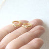Gold hoop earrings with small gemstones on a hand against a light background