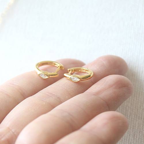 Gold hoop earrings with small gemstones on a hand against a light background