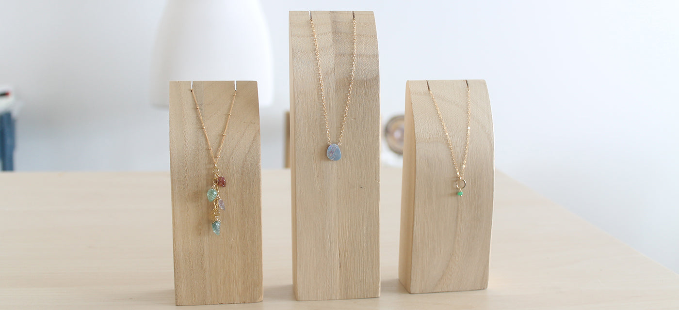 Three wooden jewelry stands with necklaces on a light surface.