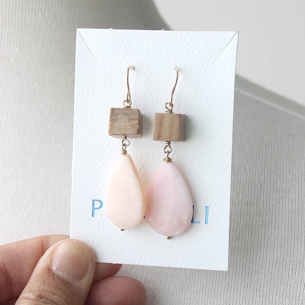 Pair of earrings with teardrop-shaped pink stones on a white card held by a hand.