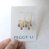 Gold earrings with green beads on a Peggy Li card held by a hand.