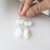White teardrop-shaped earrings with gold accents held by a hand against a light background